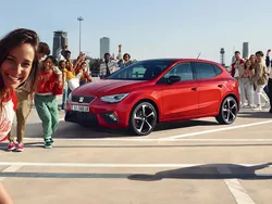 Mehrere junge Leute stehen fröhlich vor und neben einem roten Seat Ibiza