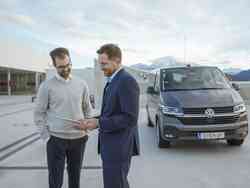 Zwei Männer unterhalten sich auf einem Parkplatz. Hinter ihnen steht ein grauer VW Bus.