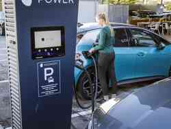 Eine Frau steckt ihr blaues Fahrzeug an einer Elektrotankstelle an.