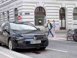 Mann und Frau gehen über die Straße, davor steht ein schwarzer VW geparkt