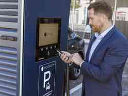 Ein Mann steht vor einem Mooncity Parkautomaten und hält sein Smartphone in der Hand.